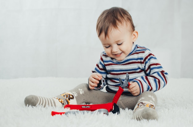 The child sits and shows a red pliers on an isolated background