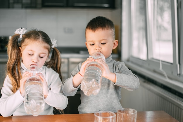 Children girl and boy drink water from liter bottles very greedily, thirsty very sweet