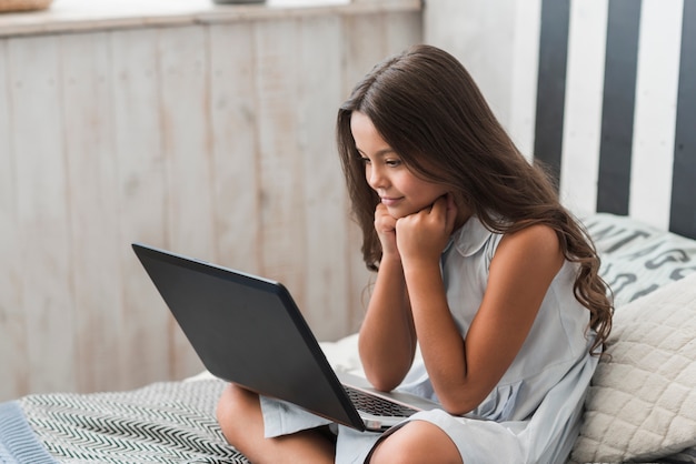 Close-up of a girl sitting on bed looking at laptop