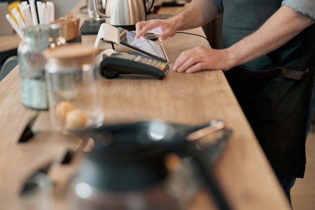 Photo close up of male barista working in cafeteria and writing order of clients