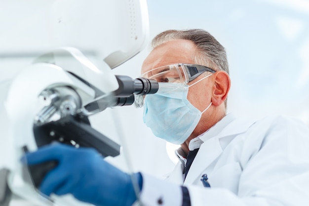 Close up. scientist in a protective mask looking through a microscope. science and health protection.