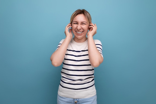 Closeup photo of a positive cheerful blond girl in a striped sweater on a blue background with copy