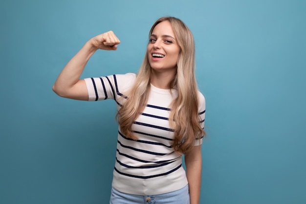 Closeup photo of a strong girl in casual clothes showing superiority with muscles on a blue isolated