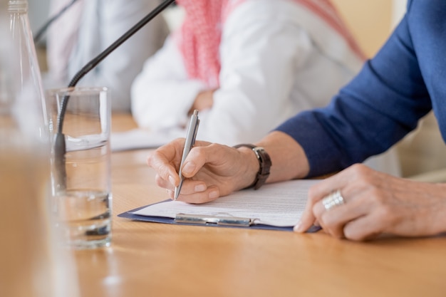 Closeup of unrecognizable woman making notes in paper while participating in conference