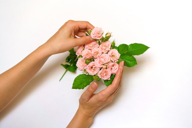 Closeup of woman florists hand making bouquet of pink roses on a light table beautiful cute bouquet ...