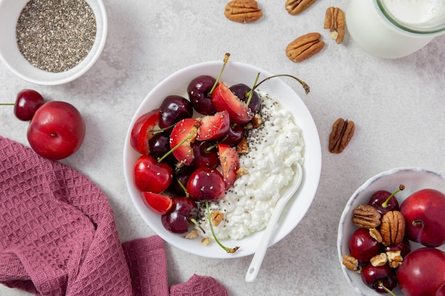 Cottage cheese with fresh cherry berries, plums, nuts, chia seeds and milk in a white bowl on a light background.