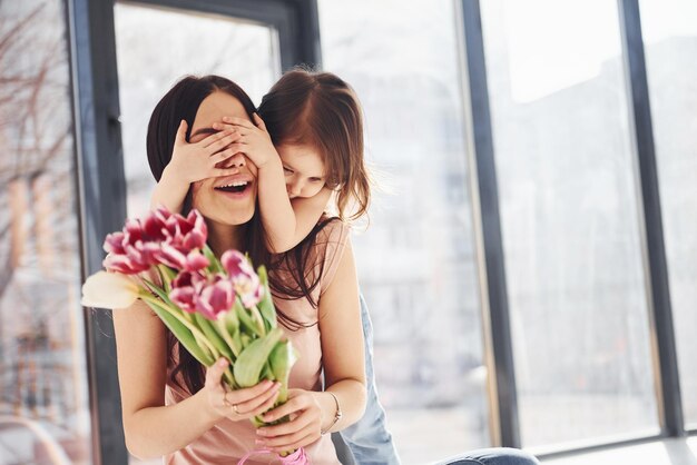 Photo covering eyes daughter congratulates mother with holiday and gives bouquet of flowers