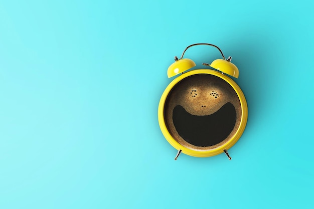 Creative coffee with a smile and a yellow alarm clock on a blue background Concept idea of a happy wake up in the morning Beginning of a successful day Top view