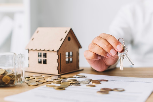 Crop hand with keys near house and coins