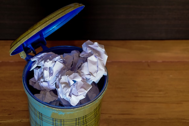 Photo crumpled paper in and out of the trash can on wood floor.