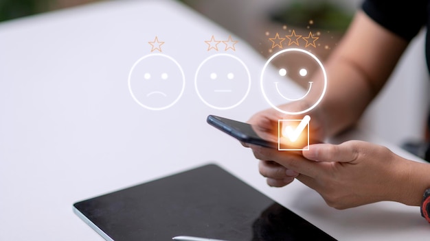 Photo customer service evaluation concept using a smartphone is pressing face emoticon smiling in satisfaction on virtual touch screen