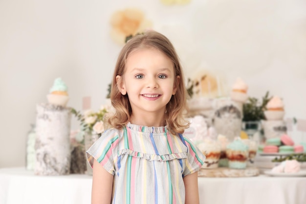 Photo cute little girl near table with sweets served for party