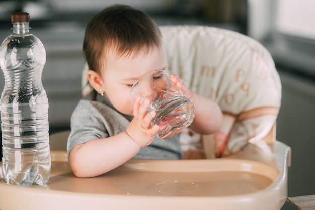 Cute little girl sitting in a baby chair in the kitchen and drinking water