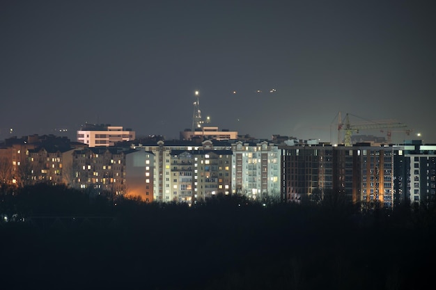 Dark silhouette of tower cranes at high residential apartment buildings construction site at night Real estate development