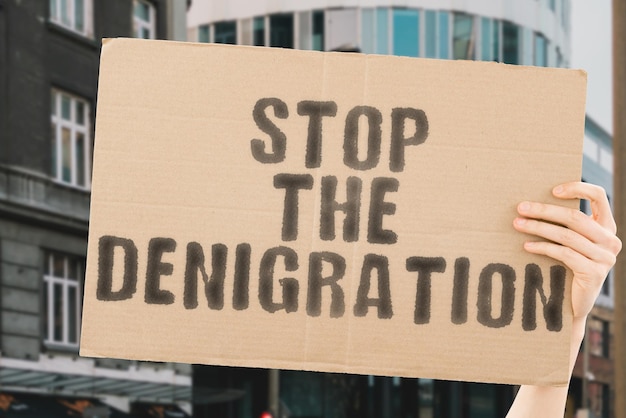 De zin "Stop de denigratie" op een spandoek in mannenhand met onscherpe achtergrond. Intimidatie. Wreedheid. Wantrouwen. Cyberpesten. Slachtoffer. Scheiding. Pijn lijden. Lijden. Trauma