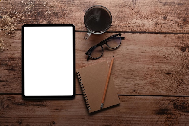 Digital tablet with blank screen coffee cup eyeglasses and notebook on wooden table