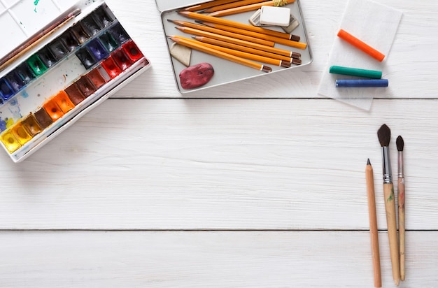 Photo drawing tools, stationary supplies, workplace of artist. watercolor paints and blank paper on white wooden desk, top view, flat lay, copy space