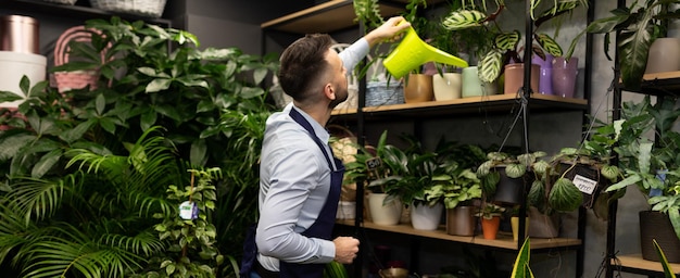 Een medewerker van een bloemenwinkel geeft vanuit een gieter de planten water in de schappen