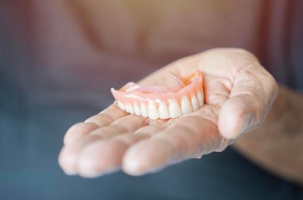 Photo an elderly man holds a denture a man is holding dentures in his hand