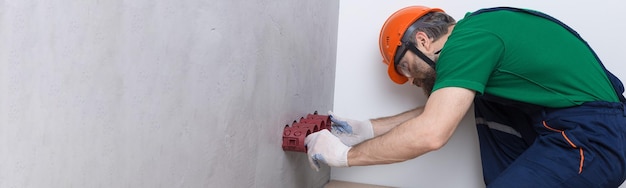 An electrician installs sockets in the apartment A guy in an orange helmet and overalls makes electrics in the house