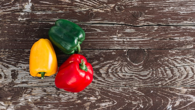 An elevated view of tri color organic bell peppers on wooden desk