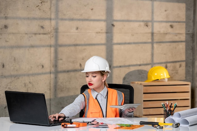 Engineer civil worker in helmet and vest smart young cute blonde girl creating plan