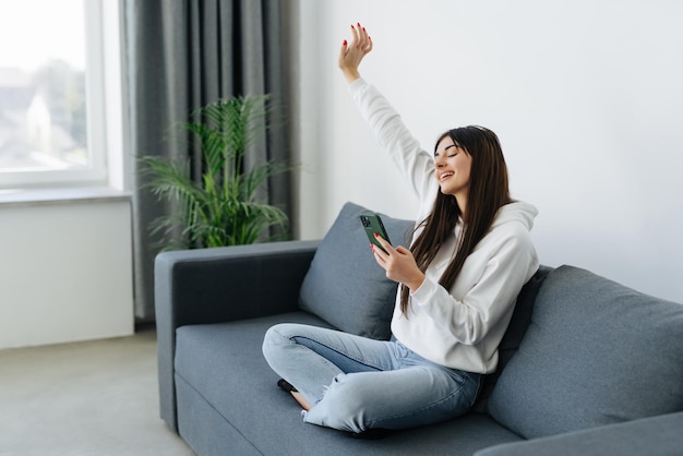 Excited woman watching media content on line in a mobile phone sitting on a couch in the living room at home