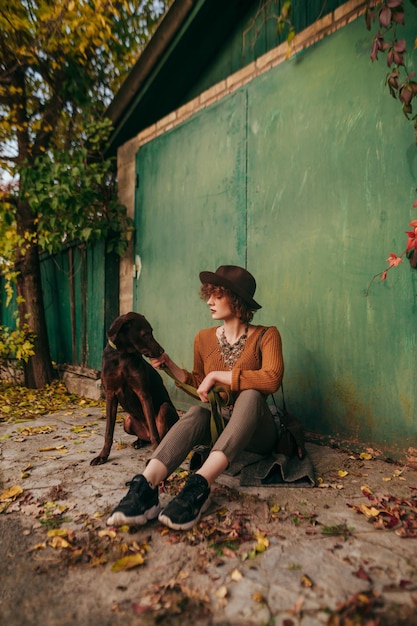 Fashion portrait of a lady sitting in the autumn on the ground on the background of the green gate