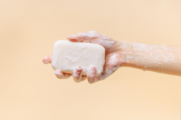 Female hand covered with foam holding natural soap on beige isolated background The concept of cleanliness selfcare and disinfection