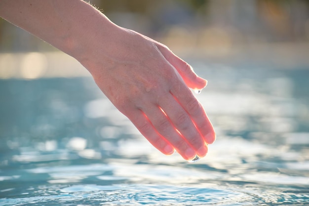 Female hand touching water of swimming pool in summer