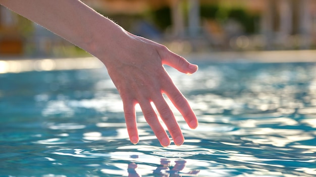 Female hand touching water of swimming pool in summer