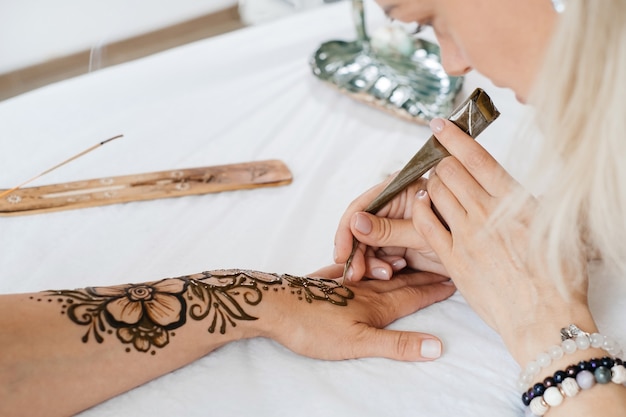 Photo female hands with mehendi pattern of flowers artist painting with henna