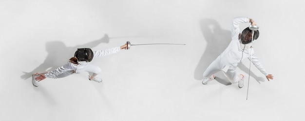 First. Teen girl in fencing costume with sword in hand on white background. Top view. Young female model practicing and training in motion, action. Copyspace. Sport, youth, healthy lifestyle. Collage.