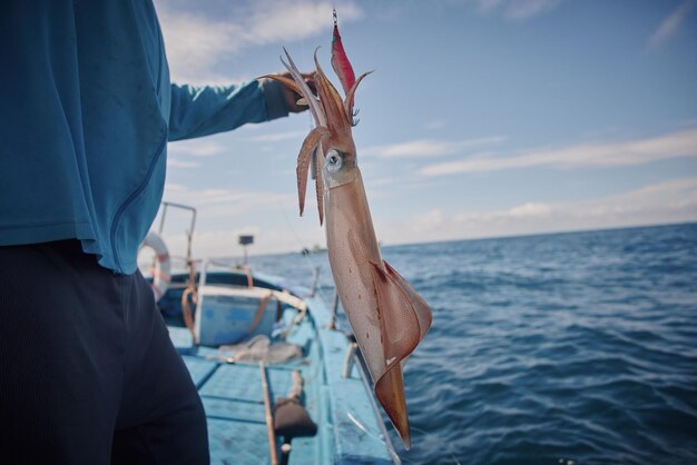 Photo fisherman standing on a boat and holding up a large squid