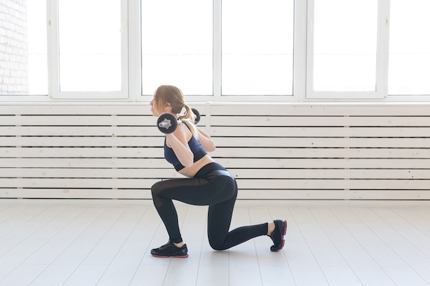 Photo fitness, sport and people concept - smiling sporty woman with barbell doing split squat or lunge.