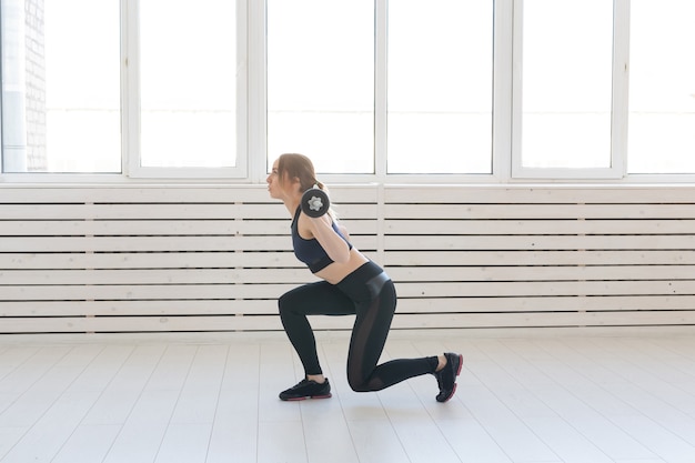 Photo fitness, sport and people concept - smiling sporty woman with barbell doing split squat or lunge.