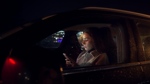 Photo focused businesswoman scrolling mobile phone in driver sits while commuting from office in luxury