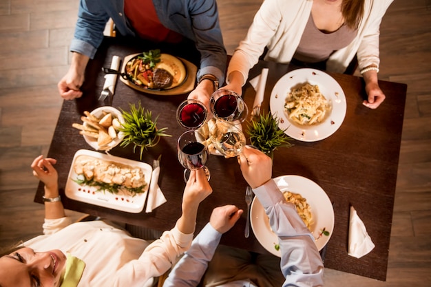 Photo four hands with red wine toasting over served table with food