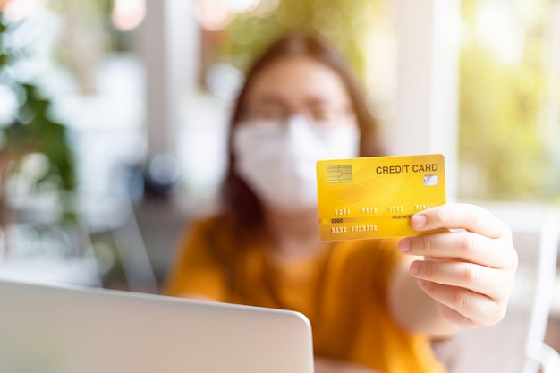 Freelance people business female wearing protective mask casual Abstract blur with focus on show holding a credit card working with laptop