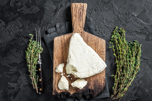 Photo fresh soft goat cheese on a cutting board with thyme. black background. top view.