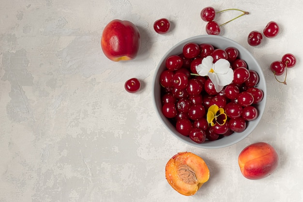 Fresh sweet cherries and nectarines decorated with flowers on grey