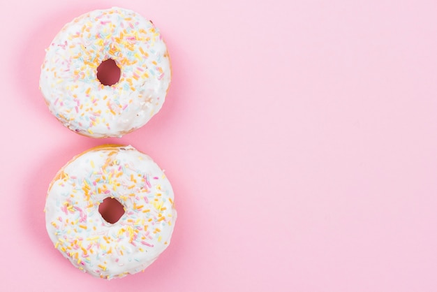 Fresh yummy white chocolate donuts on pink background