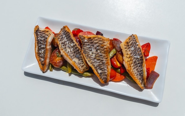 Fried fish with vegetables on a white tray traditional food from Spain on white table