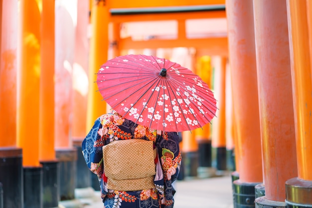 Photo 京都の伏見稲荷神社の赤い木製の鳥居の中で日本の着物を着ている芸者の女の子