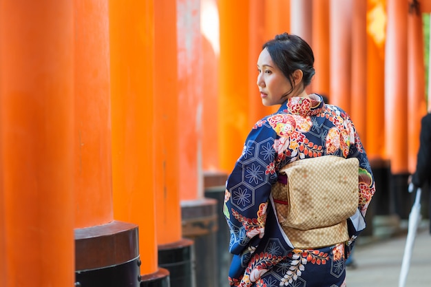 Photo 赤い木製の鳥門の中で日本の着物を着ている芸者の女の子