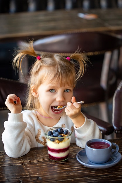 Girl eats dessert at the table. Happy child eats sweets. Beautiful baby smiling at the table. Tea party with a child. Funny girl eats ice cream. child is laughing at lunch. Beautiful girl eats