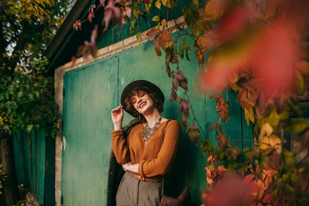 girl fashionable clothes and hat stands in autumn day against the background of grunge green wall