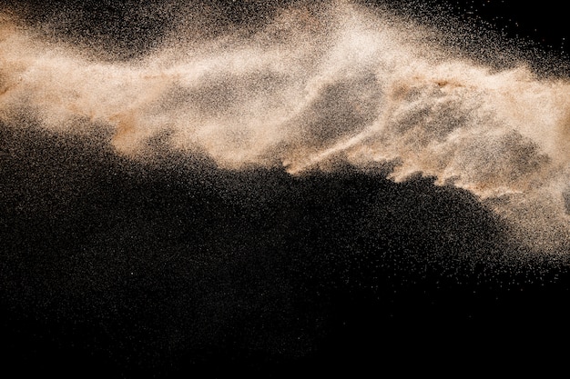 Golden colored sand splash against black background. Yellow sand fly wave in the air.