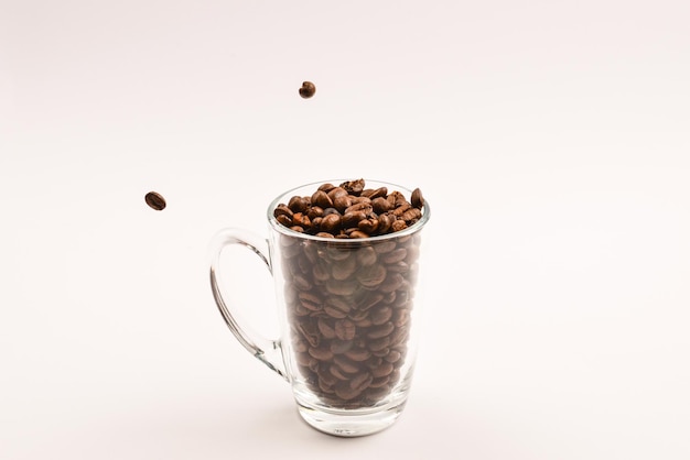 Grains of coffee are poured into a glass cup on a white background