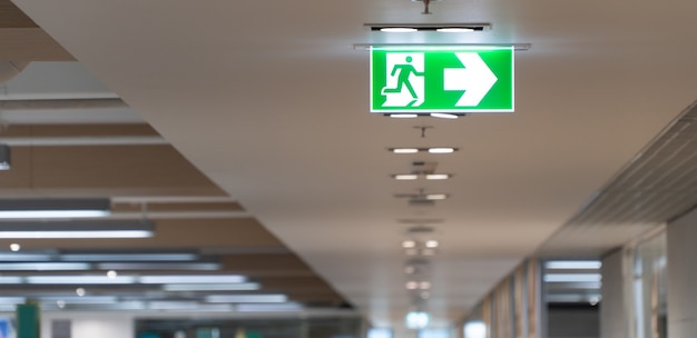 Photo green fire escape sign hang on the ceiling in the office.